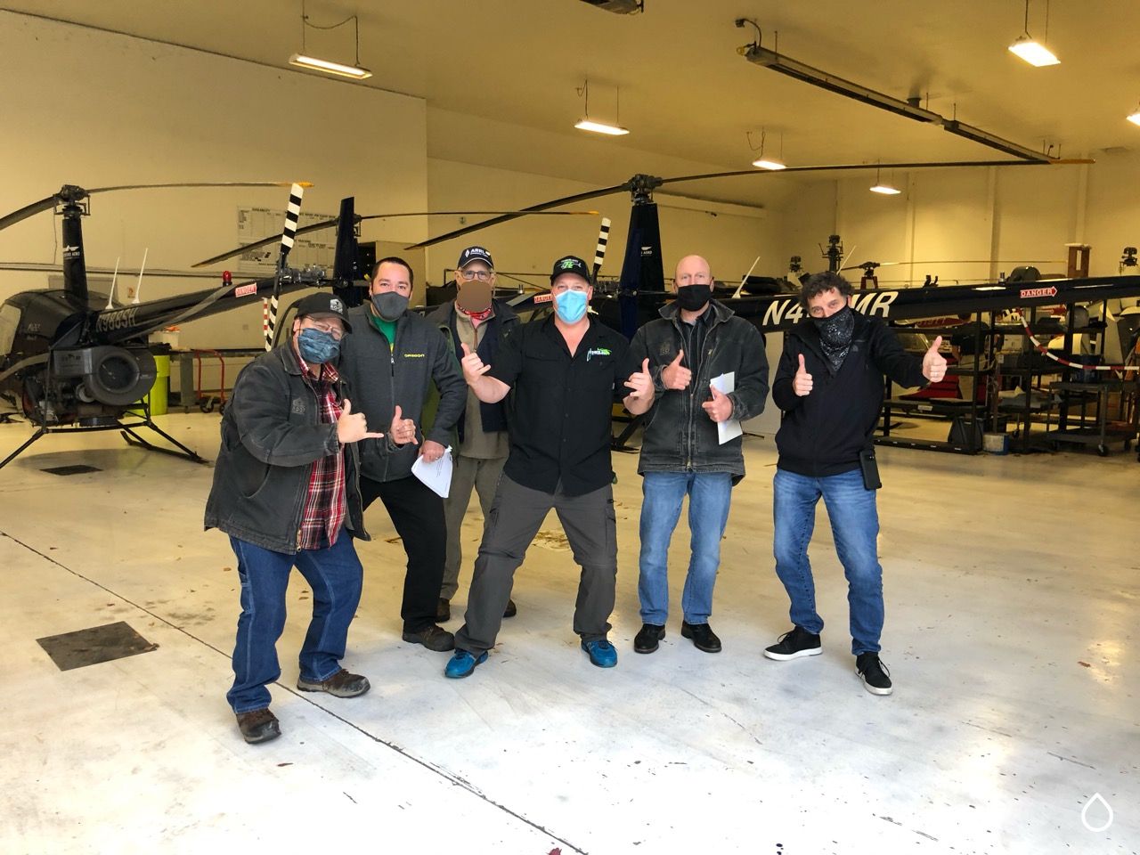 A Quantum Dynamics class group in the Timberland Helicopters hangar, students and instructors giving thumbs up in front of the helicopters