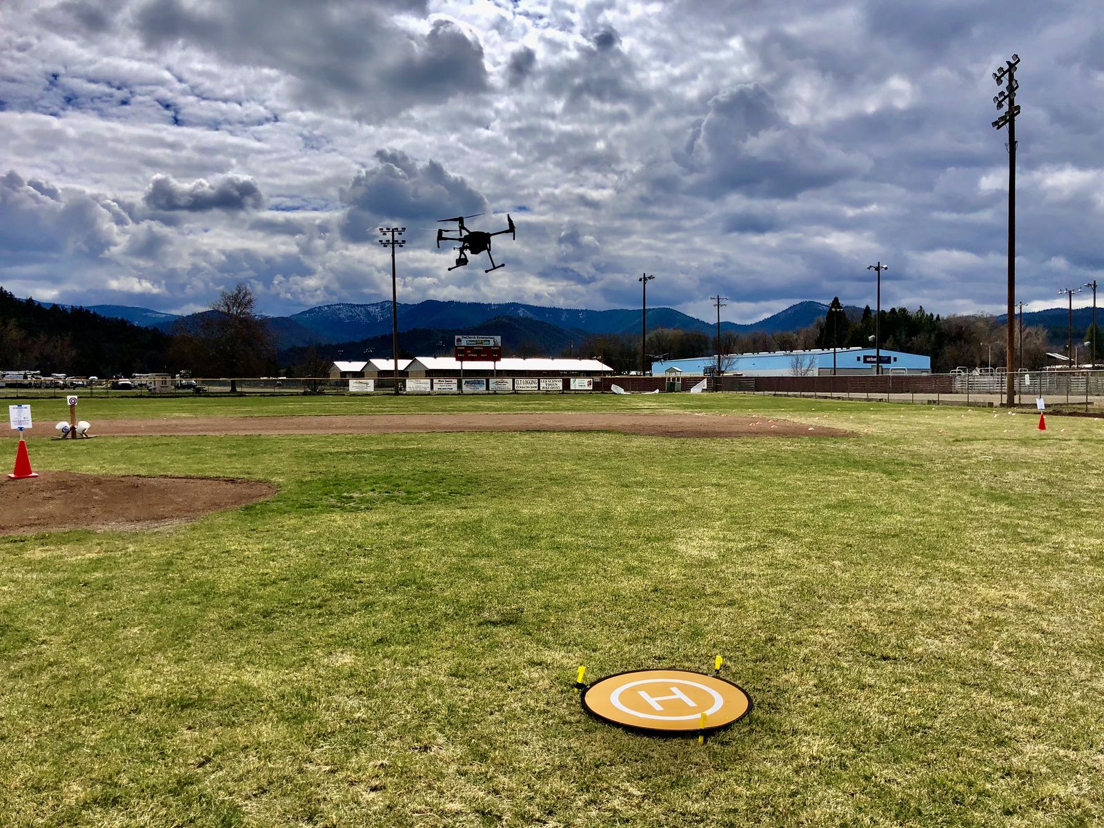 A Quantum Dynamics training drone in flight over the practice field, the orange landing pad below it and mountains behind